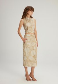 Béžová květinová dvoudílná souprava se sleeveless topem s knoflíkem a odpovídající sukní ke kolenům s bočními kapsami. Saténový povrch.