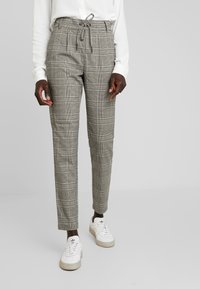 Grå rutiga byxor med dragsko i midjan, smal passform och sidofickor, kombinerade med vita sneakers. Strukturerad tyg med rutig mönster.