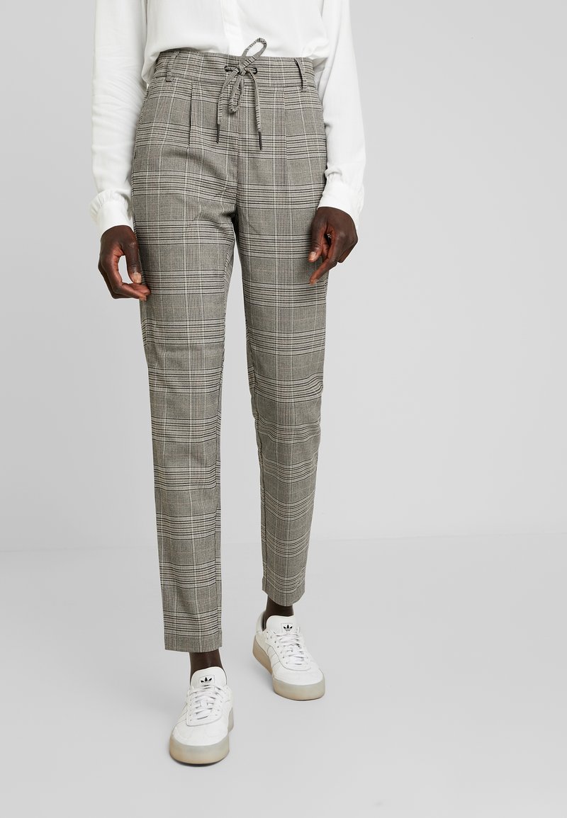 Grå rutiga byxor med dragsko i midjan, smal passform och sidofickor, kombinerade med vita sneakers. Strukturerad tyg med rutig mönster.