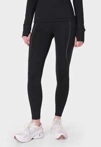 Zwarte sportleggings met een slanke pasvorm, voorzien van contrasterende grijze stiksel en een soepele textuur, gecombineerd met witte hardloopschoenen.