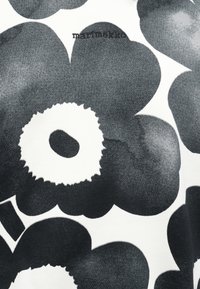 Crno-bijela tkanina s velikim cvjetnim uzorkom, gusto teksturiranim laticama i tekstom "marimekko" blizu vrha u sredini.