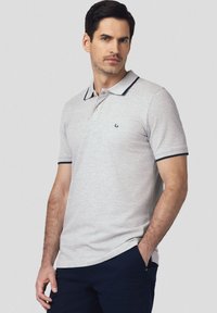 Szary polo z wąskim kolorem w granatowym odcieniu i akcentami na rękawach. Posiada trzy guziki przy szyi oraz małe logo na klatce piersiowej.