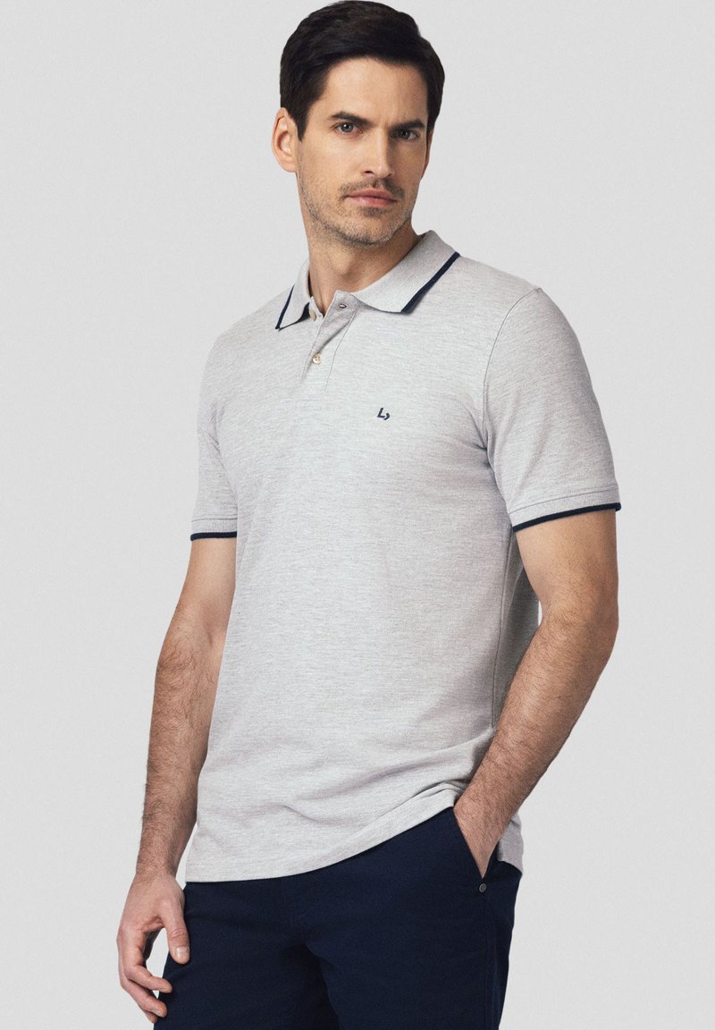 Szary polo z wąskim kolorem w granatowym odcieniu i akcentami na rękawach. Posiada trzy guziki przy szyi oraz małe logo na klatce piersiowej.