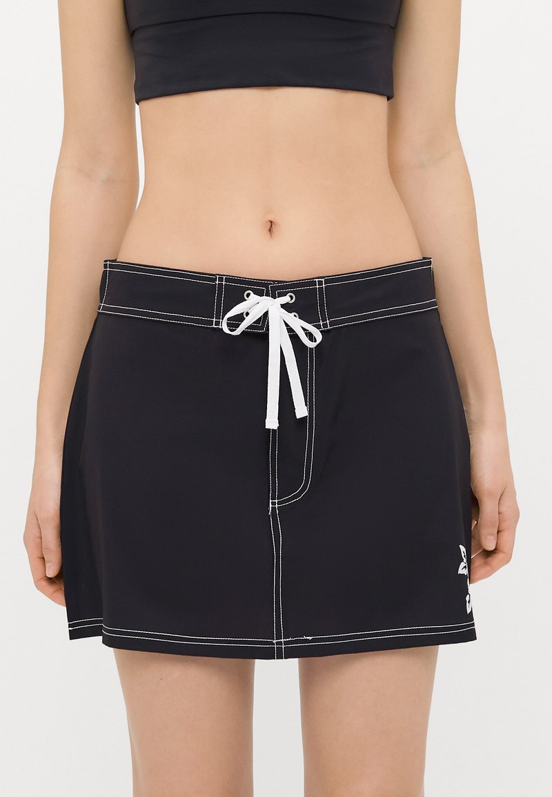 Falda de baño negra con cordón blanco, con costuras blancas y detalle de logo en el lateral, fabricada con material ligero y de secado rápido.