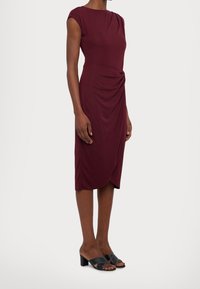 Burgundy klänning med figursydd passform och korta ärmar, sidodrapering, knälång skärning. Kombination med svarta sandaler med öppen tå och klack.