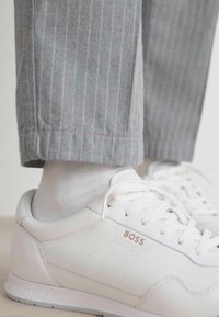 Hvite lær sneakers har en glatt tekstur, snøring og subtil merking. Kombinert med lysegrå stripete bukser.