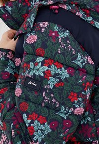 Blommig puffjacka med marin bakgrund och flerfärgade blommor. Kviltat mönster och tygmärke på ärmen.