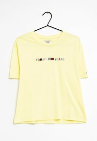 Žluté bavlněné tričko s krátkým rukávem, s textem "TOMMY JEANS" v barevných písmenech a kontrastním logem na rukávu.