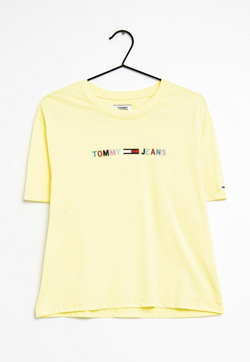Žluté bavlněné tričko s krátkým rukávem, s textem "TOMMY JEANS" v barevných písmenech a kontrastním logem na rukávu.