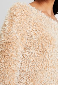 Maglione beige fuzzy con un tessuto a lunga peluria, caratterizzato da un design off-shoulder e un aspetto morbido e soffice.