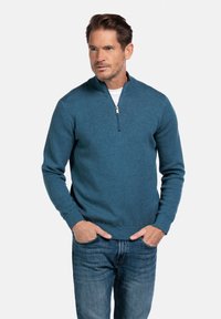 Navyblauwe pullover met rits, gemaakt van zacht, textuurgebreid materiaal. Beschikt over lange mouwen en een aangesloten ontwerp. Gecombineerd met denim jeans.