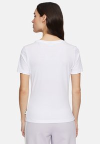Witte kortaf t-shirt met een ronde halslijn. Zacht katoen met een gladde textuur. Etiket zichtbaar aan de onderkant links. Eenvoudig ontwerp.