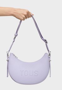 Borsa in pelle lilla dalla forma a mezzaluna, con logo "TOUS" impresso e tracolla regolabile con accessori in argento.