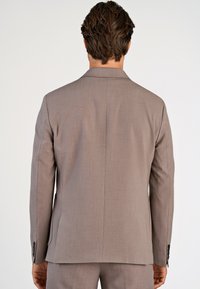 Marynarka w jasnobrązowym kolorze o gładkiej fakturze, z pojedynczym rozcięciem i klapami z wycięciem. Posiada czarne guziki na mankietach oraz dopasowany krój.