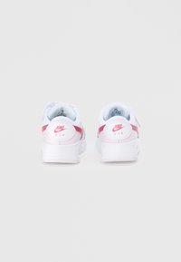 Nike Air tenisky s bielym zvrškom, ružovými akcentmi a viditeľným odpružením päty. Majú okrúhle logo na päte a textúrovanú podrážku.