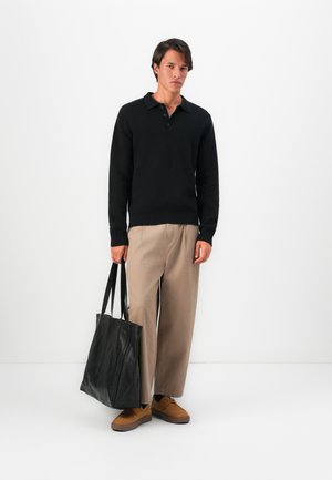 Black knitted pullover with a collar and three buttons, paired with beige wide-leg trousers and brown shoes, holding a large black tote bag.
