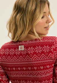 Czerwony longsleeve z długim rękawem z białym wzorem płatków śniegu, z metką z tyłu. Wykonany z miękkiego materiału o dopasowanym kroju.