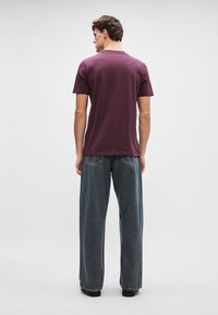 Burgundy lühikeste varrukatega T-särk ümmarguse kaelusega, koos laia lõikega pleekinud siniste teksadega, jalas mustad kingad.