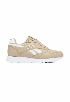 Zapatilla beige de Reebok con detalles blancos, cierre de cordones y suela acolchada blanca, mostrada de lado sobre un fondo blanco.