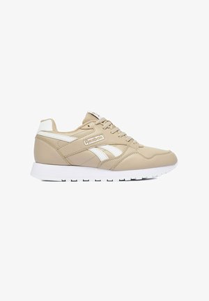 Beiger Reebok Sneaker mit weißen Akzenten, Schnürverschluss und weißer gepolsterter Sohle, von der Seite auf weißem Hintergrund gezeigt.