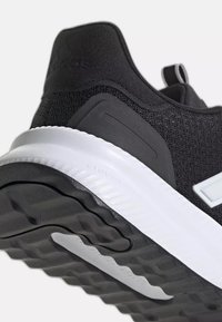 Gros plan sur le talon et la semelle d'une chaussure de sport noire et blanche avec une semelle texturée et une tige en mesh.
