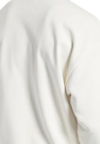 Světle béžová látka, mikina s kulatým výstřihem a jemnou strukturou. Trochu oversized střih, s kleslými rameny a minimem švů.