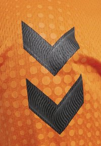Oranje stof heeft een gestructureerd, gestippeld patroon met een opvallend zwart zigzagontwerp, dat de golfstructuur op de accenten benadrukt.