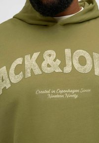 Oliwkowa bluza z kapturem z teksturowanym białym nadrukiem z napisem "BACK&JO" oraz "Created in Copenhagen Since Nineteen Ninety" w dyskretnym kroju czcionki.