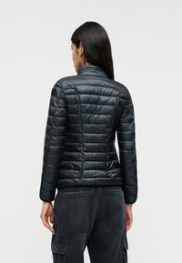 Μ αύρο μπουφάν puffer με ψηλό γιακά, υφή με ραφές σε σχήμα καπιτονέ και εφαρμοστή σχεδίαση. Διαθέτει λεία, γυαλιστερή επιφάνεια και διακριτικές διακοσμητικές ραφές.