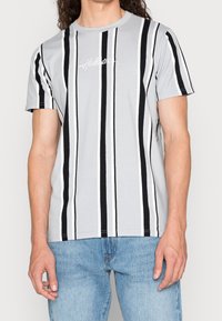 Grå kortärmad t-shirt med vertikala svart- och vitrandiga mönster och en vit broderad logotyp på bröstet.