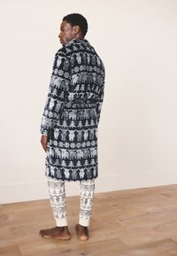 Granatowy szlafrok z białymi wzorami zwierząt i płatków śniegu, wykonany z pluszowej tkaniny; do niego dołączone białe spodnie do piżamy z podobnymi wzorami.