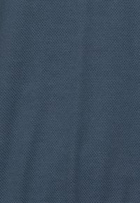 Dunkelblaues, strukturiertes Gewebe mit einem gewebten Muster, das ein wabenähnliches Design zeigt. Das Material wirkt atmungsaktiv und leicht dehnbar.