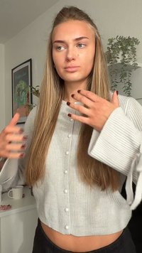 Grijze, geribbelde, gebreide cropped cardigan met lange mouwen en knopen aan de voorkant. Model met lang haar, toont zwarte broek en een neutrale achtergrond.