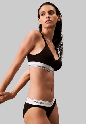 Svart bomull bralette og matchende truser med hvit Calvin Klein-logo på linningen, glatt tekstur og minimalistisk design.