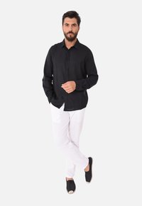 Camicia nera a maniche lunghe con bottone davanti, abbinata a pantaloni in lino bianchi e espadrilles nere con punta beige.