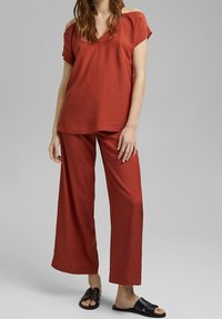 Top rojo de corte suelto con mangas cortas y escote en V, combinado con pantalones de pierna ancha en el mismo color. Sandalias planas negras completan el conjunto.