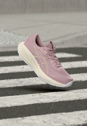 Ροζ αθλητικό παπούτσι στον αέρα πάνω από διάβαση πεζών σε άσφαλτο, με σωματίδια βρωμιάς να πετάνε κάτω από τη σόλα.