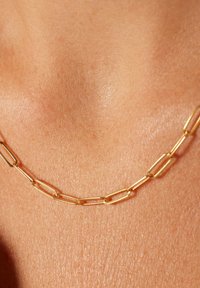 Gouden ketting met verlengde, rechthoekige schakels met een gladde textuur, rustend tegen de huid, wat de eenvoud van het design benadrukt.