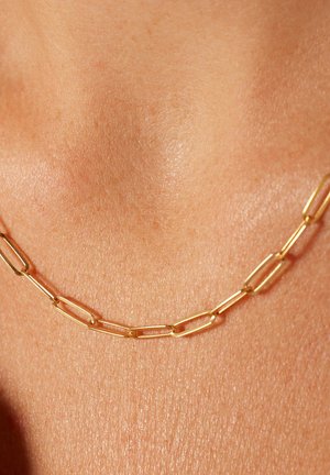 Collier en or avec des maillons rectangulaires allongés à la texture lisse, reposant contre la peau, mettant en avant la simplicité du design.