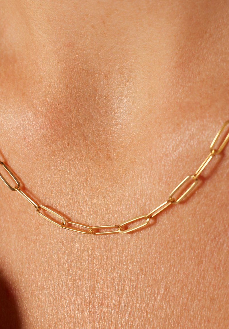 Gouden ketting met verlengde, rechthoekige schakels met een gladde textuur, rustend tegen de huid, wat de eenvoud van het design benadrukt.