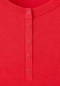 Tissu tricoté rouge avec encolure ronde côtelée et une rangée verticale de cinq petits boutons ronds au centre devant.