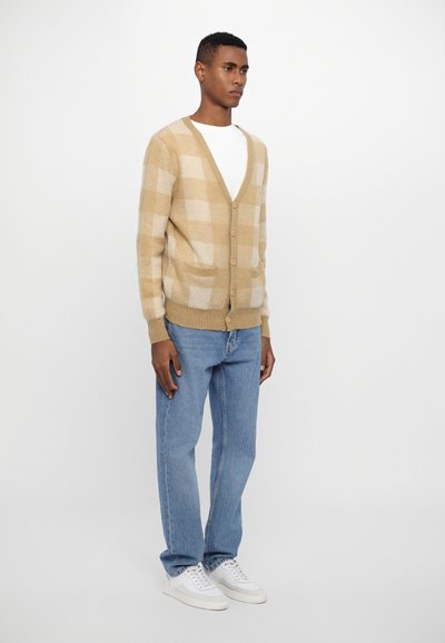 Beige och krämfärgad randig cardigan med V-hals, knäppning och fickor, i kombination med ljusblå raka jeans och vita sneakers.