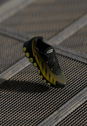 Adidași sport în nuanțe de negru și galben, cu un superior texturat, design din plasă și o talpă distinctivă cu bule, evidențiată de accente verzi. Logo-ul Nike este vizibil.
