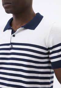 Marineblauwe en witte gestreepte polo shirt, met een volle marineblauwe kraag, korte mouwen en een knoopsluiting met drie knopen. Glad breiwerk.