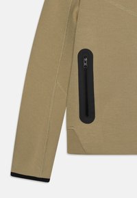 Khaki dlouhý rukáv z texturované látky se černou kapsou na zip na levém rukávu a kontrastními černými manžetami.