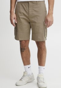 Khaki színű cargo rövidnadrág oldalsó zsebekkel, pamut anyagból készült. Egyenes szabású és lapos derékpánttal rendelkezik. Fehér Nike zoknikkal és sportcipőkkel viselik.