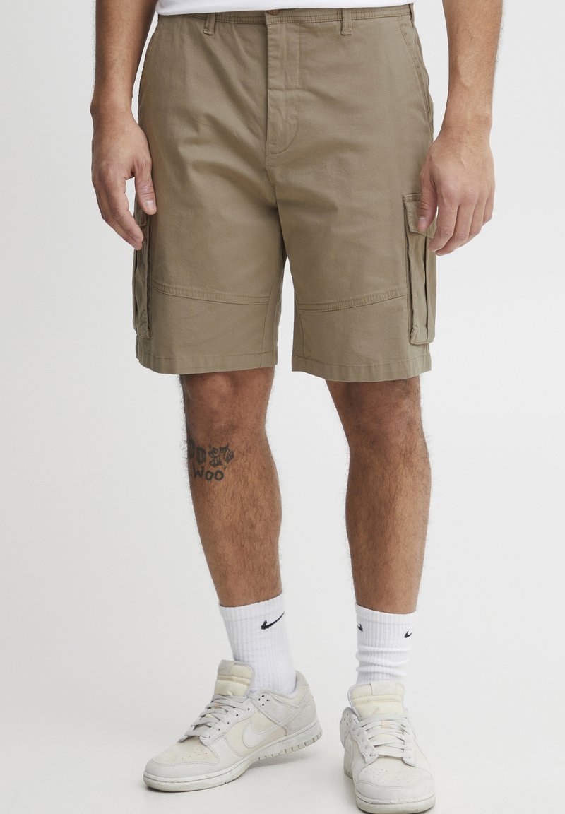Khaki színű cargo rövidnadrág oldalsó zsebekkel, pamut anyagból készült. Egyenes szabású és lapos derékpánttal rendelkezik. Fehér Nike zoknikkal és sportcipőkkel viselik.