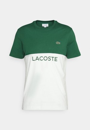 Short-sleeve Lacoste t-shirt, green upper half, white lower half with "LACOSTE" text and small crocodile logo on chest.