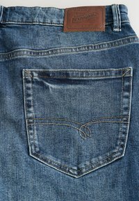 Jeansy dżinsowe w głębokim niebieskim kolorze, z tylną kieszenią z kontrastującym przeszyciem oraz brązową skórzaną metką na pasku od spodni.