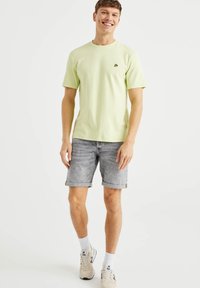 Ljust grön bomullströja med korta ärmar och rund hals, matchad med ljusgrå denimshorts som är uppvikta vid fållen. Casual sneakers på fötterna.
